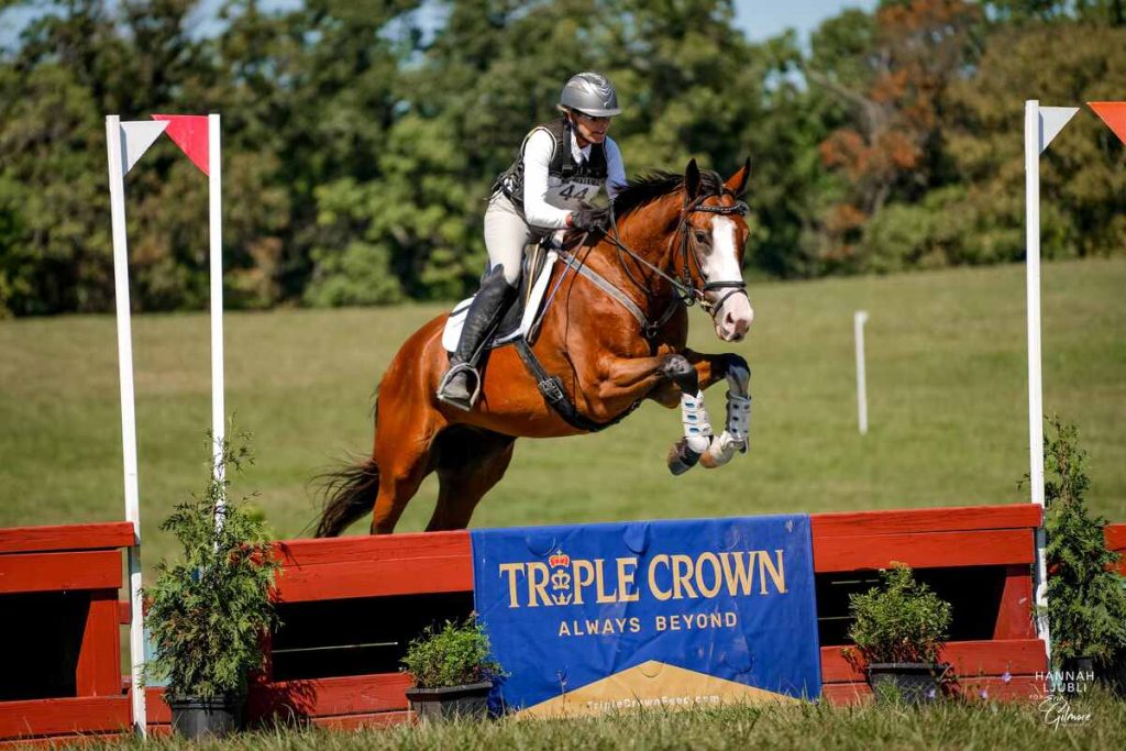 Horse and rider jumping a cross county fence with Triple Crown banner