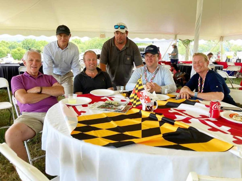 Group of men and a woman sitting at table with Maryland International Flag