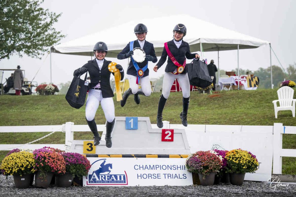 Three riders jumping off podium, holding awards.